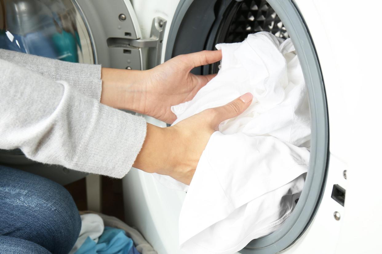 female hands getting out white clean clothes from washing machine