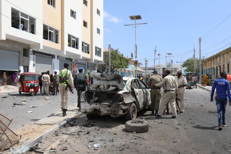 Somali policemen assess the wreckage of a car, destroyed at the scene of a bomb explosion in Mogadishu