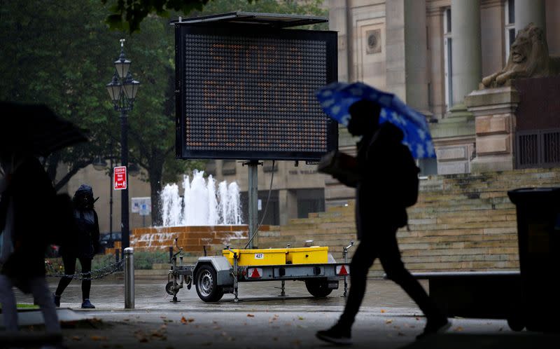 People walk past an information board following the outbreak of the coronavirus disease (COVID-19) in Bolton, Britain