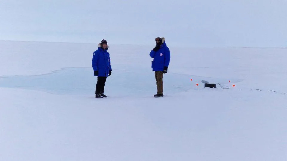 Dos investigadores envueltos en equipo ártico mientras observan la bomba de agua de mar en acción.