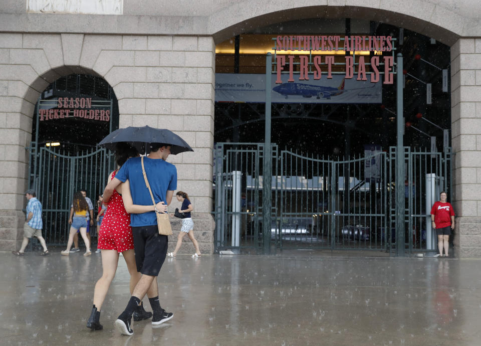 Fans arrive to closed gates at Globe Life Park as a heavy rain begins to fall for a scheduled baseball game between the Los Angeles Angels and Texas Rangers in Arlington, Texas, Monday, July 1, 2019. The teams postponed the game to an unknown date following the death of Angels pitcher Tyler Skaggs. (AP Photo/Tony Gutierrez)