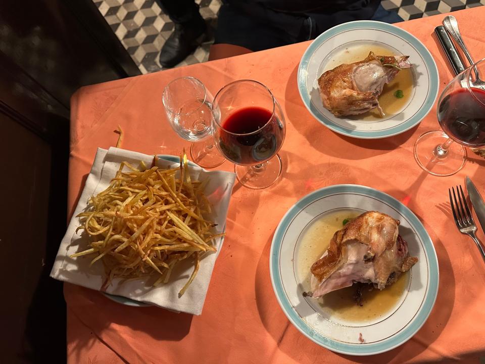 Plated pieces of roast chicken at Chez L'Ami Louis next to stack of shoestring fries on table