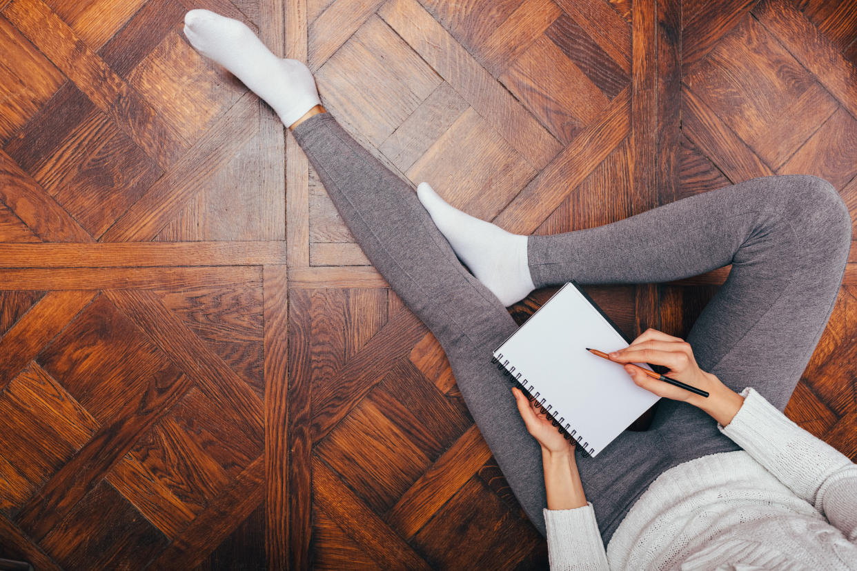 Concept of comfortable work at home. View from above woman relaxing sitting on wooden floor writing in notepad.