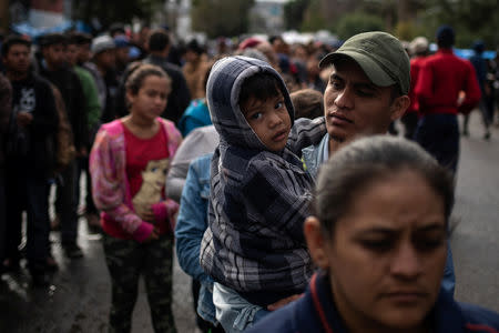 A migrant, part of a caravan of thousands from Central America trying to reach the United States, holds his son as they await in line to receive food outside a shelter in Tijuana, Mexico November 29, 2018. REUTERS/Adrees Latif