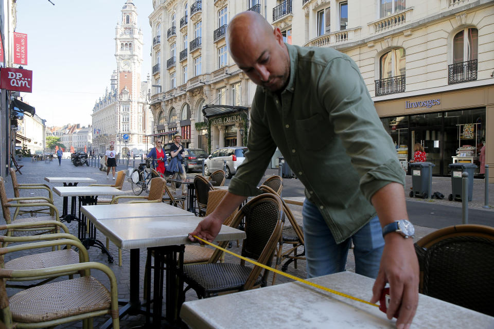 A man measures the distance between tables to respect social distance at a cafe terrace in Lille, northern France, Tuesday June 2, 2020. The French way of life resumes Tuesday with most virus-related restrictions easing as the country prepares for the summer holiday season amid the pandemic. Restaurants and cafes reopen Tuesday with a notable exception for the Paris region, the country's worst-affected by the virus, where many facilities will have to wait until June 22 to reopen. (AP Photo/Michel Spingler)