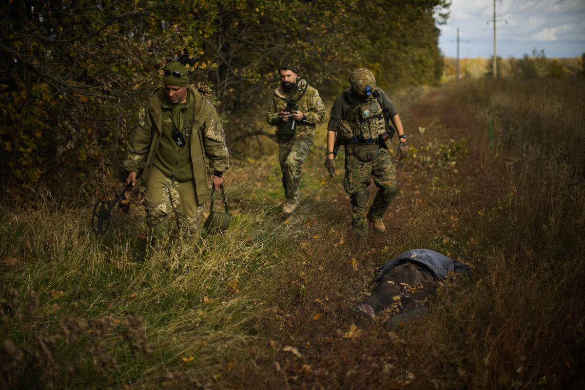 Un hombre con uniforme militar y chaleco antibalas trabaja en el bosque con  un detector de metales.