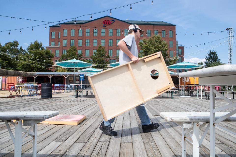 A worker sets up a Cornhole board at Constitution Yards along the Riverfront Wilmington, Thursday, Aug. 17, 2023. Constitution Yards is a seasonal beer garden offering food, drink, live music, sports on a big screen, games, beach sand, and axe throwing.