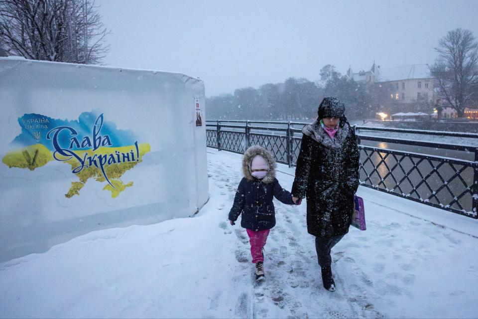 A woman and a child walk along the bank of the Uzh river during heavy snowfall in far western Ukraine (REUTERS)