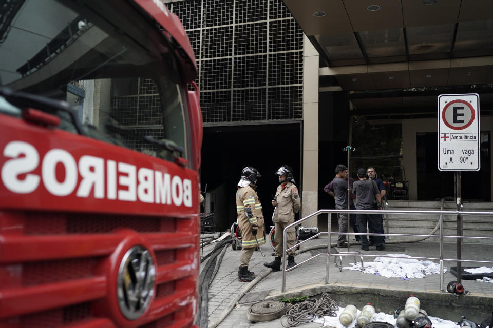 Firefighters and investigators stand at the entrance of the Badim Hospital, where a fire left at least 11 people dead, in Rio de Janeiro, Brazil, Friday, Sept. 13, 2019. The fire raced through the hospital forcing staff to wheel patients into the streets on beds or in wheelchairs. (AP Photo/Leo Correa)