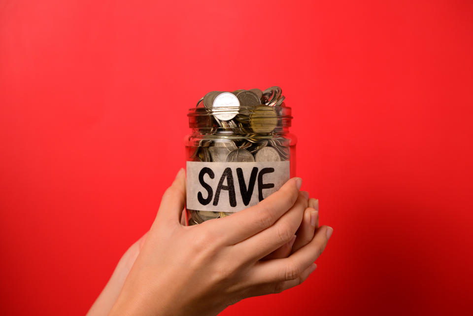 Hands holding a jar filled with coins labeled "SAVE" against a solid background