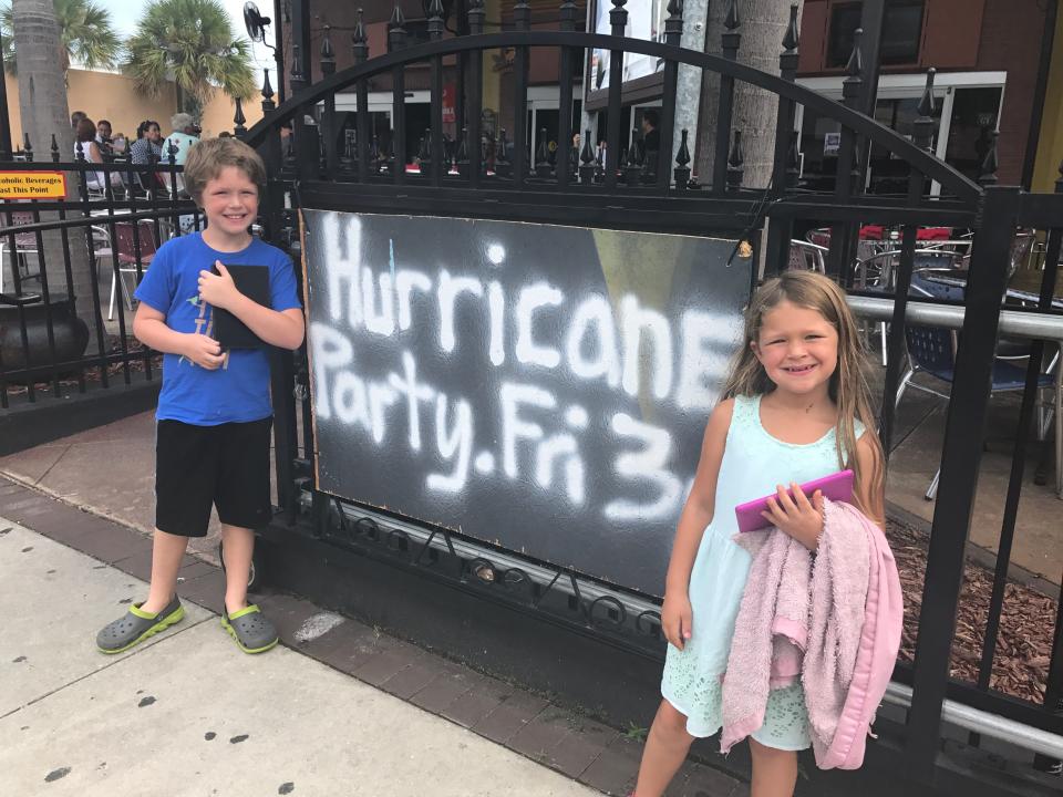hurricane party fri 3 spray-painted on wood panel on a fence with two kids standing next to it