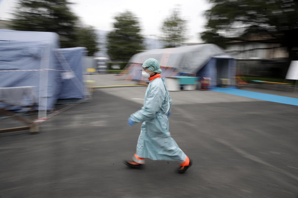 FILE - In this Thursday, March 12, 2020 file photo, a worker wearing a mask and protective clothing walks between the emergency structures that were set up to ease procedures at the Brescia hospital in northern Italy. As Italy prepares to emerge from the West’s first and most extensive coronavirus lockdown, it is increasingly clear that something went terribly wrong in Lombardy, the hardest-hit region in Europe’s hardest-hit country. (AP Photo/Luca Bruno)