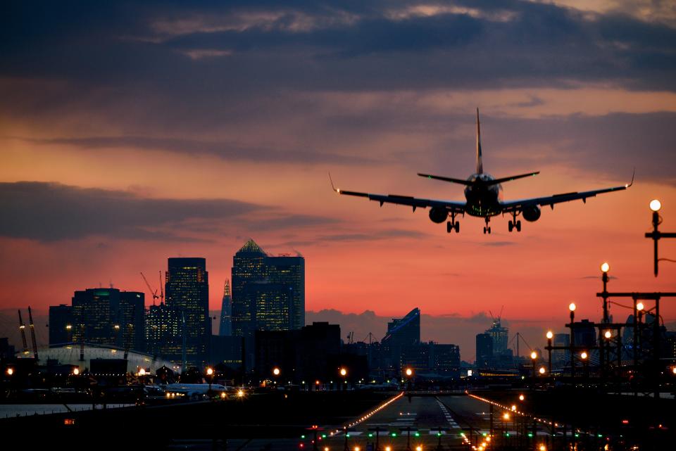 Plane takes off from runway at sunset buildings in background