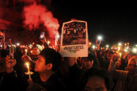 Soccer fans light a flare during a candle light vigil for the victims of Saturday's stampede, in Yogyakarta, Indonesia, Tuesday, Oct. 4, 2022. Police firing tear gas inside a stadium in East Java on Saturday in an attempt to stop violence after an Indonesian soccer match triggered a disastrous crush of fans making a panicked, chaotic run for the exits, leaving at a number of people dead, most of them trampled upon or suffocated. Writing on the poster reads "Investigate thoroughly". (AP Photo/Slamet Riyadi)