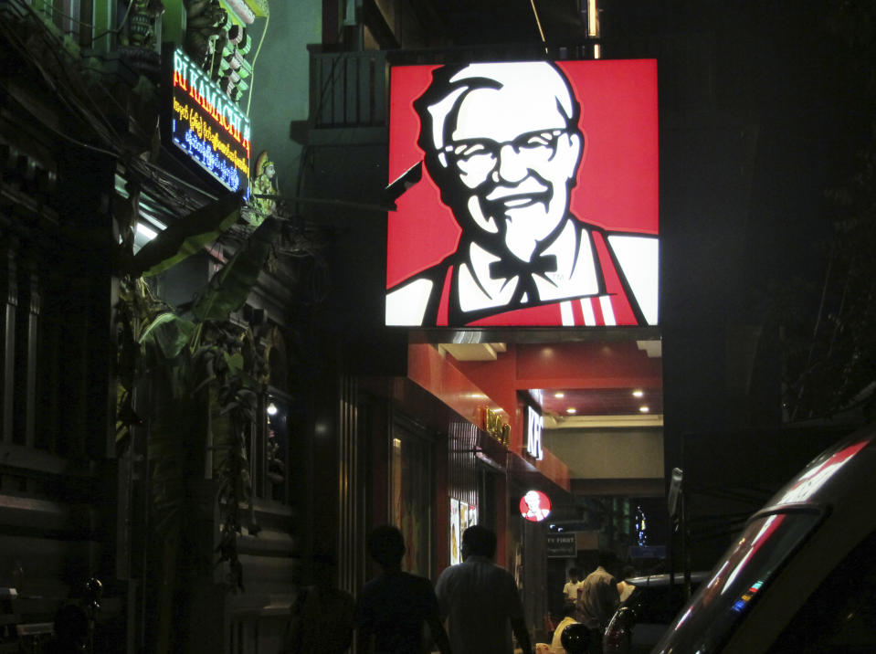FILE - In this Oct. 7, 2016, file photo, a sign of KFC's grinning Colonel Sanders and his goatee is lit outside its outlet in Yangon, Myanmar. The military coup in Myanmar is unlikely to do the country’s struggling economy any good at all. The country once considered a promising last frontier has languished as the pandemic added to its challenges. (AP Photo/Elaine Kurtenbach, File)
