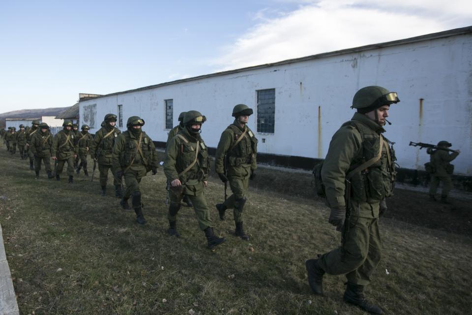 Military personnel, believed to be Russian servicemen, walk outside the territory of a Ukrainian military unit in the village of Perevalnoye outside Simferopol