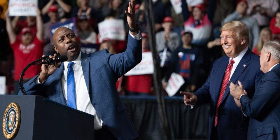 Sen. Tim Scott gestures from the presidential podium during a speech with then-President Donald Trump looking on and pointing.