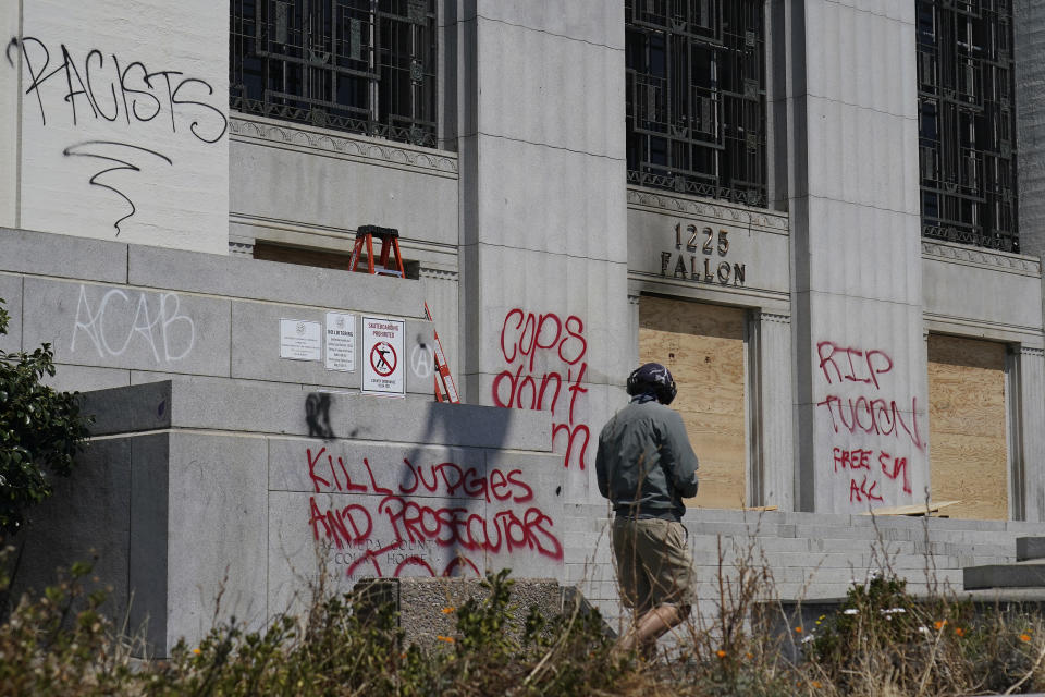 A man looks toward wooden boards and graffiti outside of the Alameda County Courthouse in Oakland, Calif., Sunday, July 26, 2020. A protest through the streets of downtown Oakland, California, in support of racial justice and police reform turned violent when "agitators" among the demonstrators set fire to a courthouse, vandalized a police station and shot fireworks at officers, authorities said. (AP Photo/Jeff Chiu)