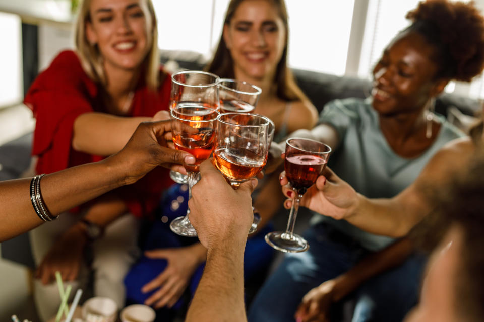 High angle view of diverse group of young friends cheering with glasses of fruit wine during a fun birthday party celebration.