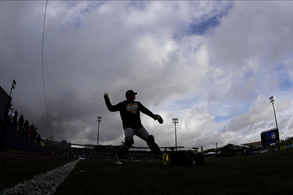 Oakland Athletics catcher Chris Herrmann is silhouetted against storm clouds as he warms up before a spring training baseball game against the Seattle Mariners, Friday, Feb. 22, 2019, in Peoria, Ariz. (AP Photo/Charlie Riedel)