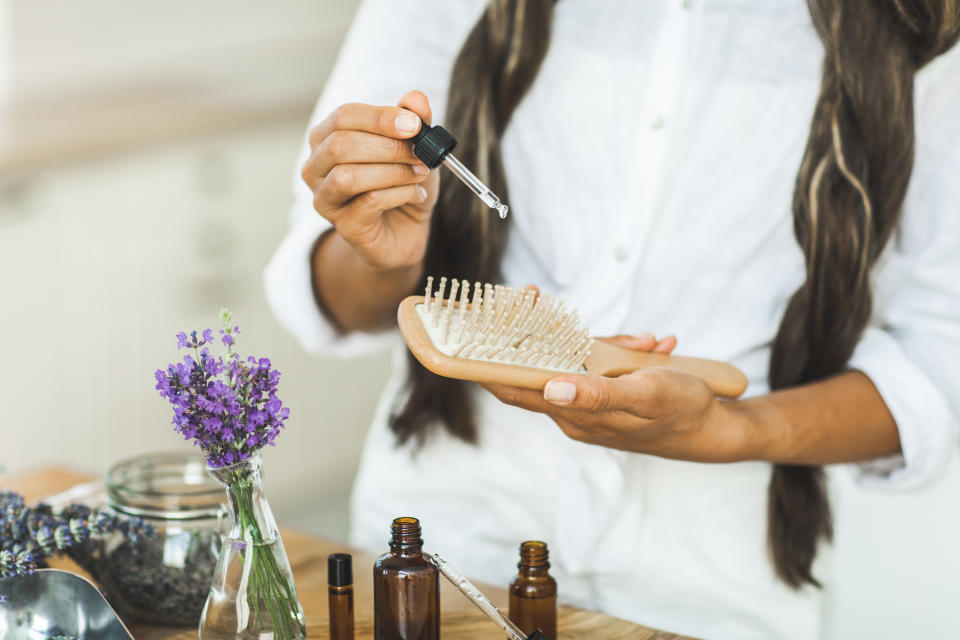 Organic hair care lavender oil bottles and wooden comb for hair care. Process of moisturizing hair. Cosmetic oil in brown amber dropper bottle, for homemade cosmetic, hair or body treatment.