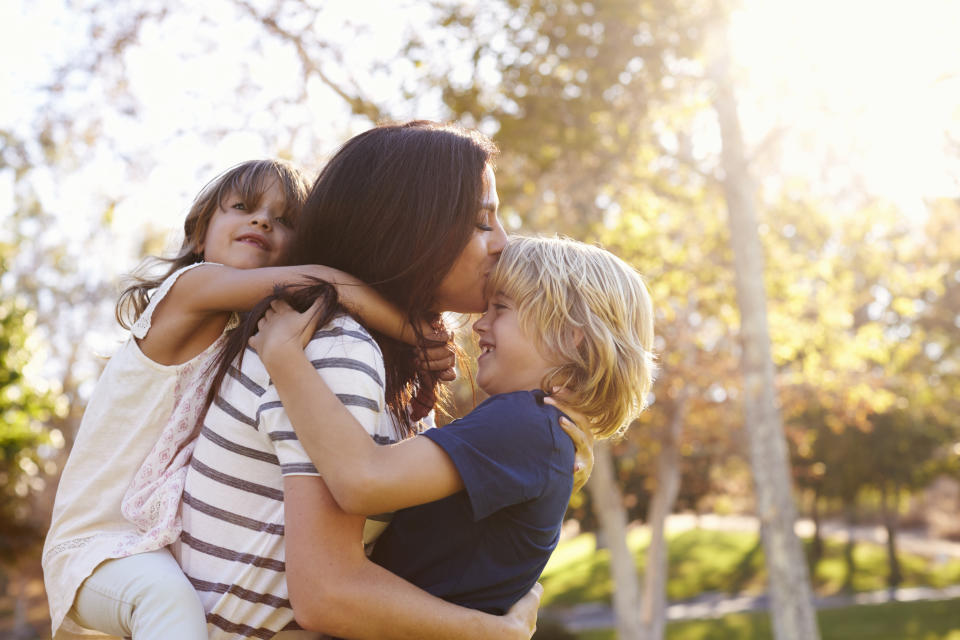 Mother Carrying Son And Daughter As They Play In Park