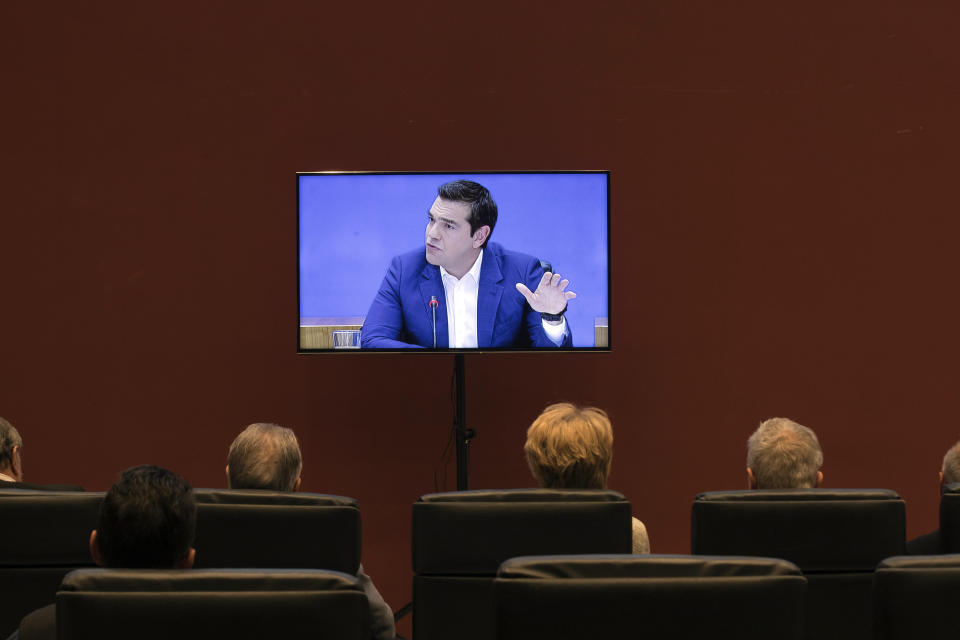 People watch a TV screen as Greek Prime Minister Alexis Tsipras announces bailout relief measures during a press conference, in Athens, on Tuesday, May 7, 2019. Greece's left-wing prime minister has promised crisis-weary voters a series of tax-relief measures ahead of elections, after outperforming budget targets set by bailout creditors. (AP Photo/Petros Giannakouris)