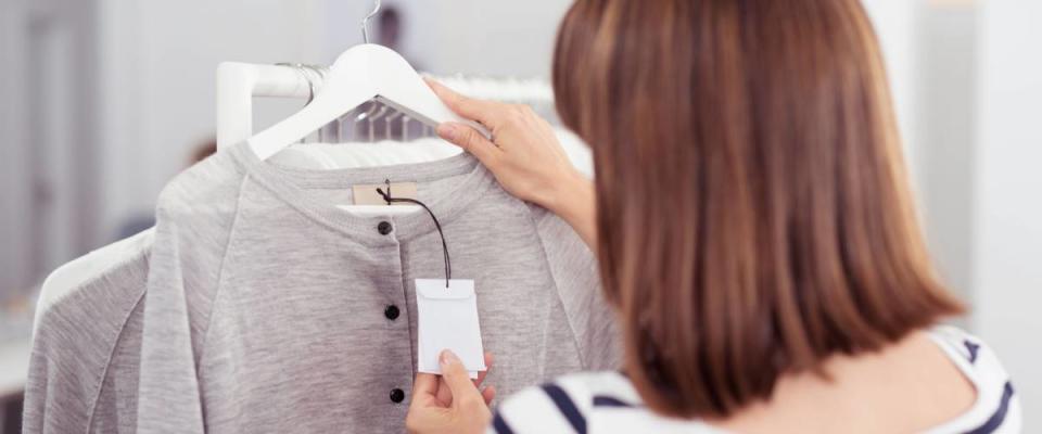 Close up Rear View of Woman Looking at the Price Tag of a Trendy Gray Shirt Hanged on Rail Inside the Clothing Store.