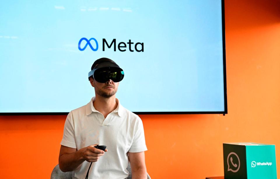 A volunteer wears virtual reality (VR) glasses in front of a TV that says Meta.