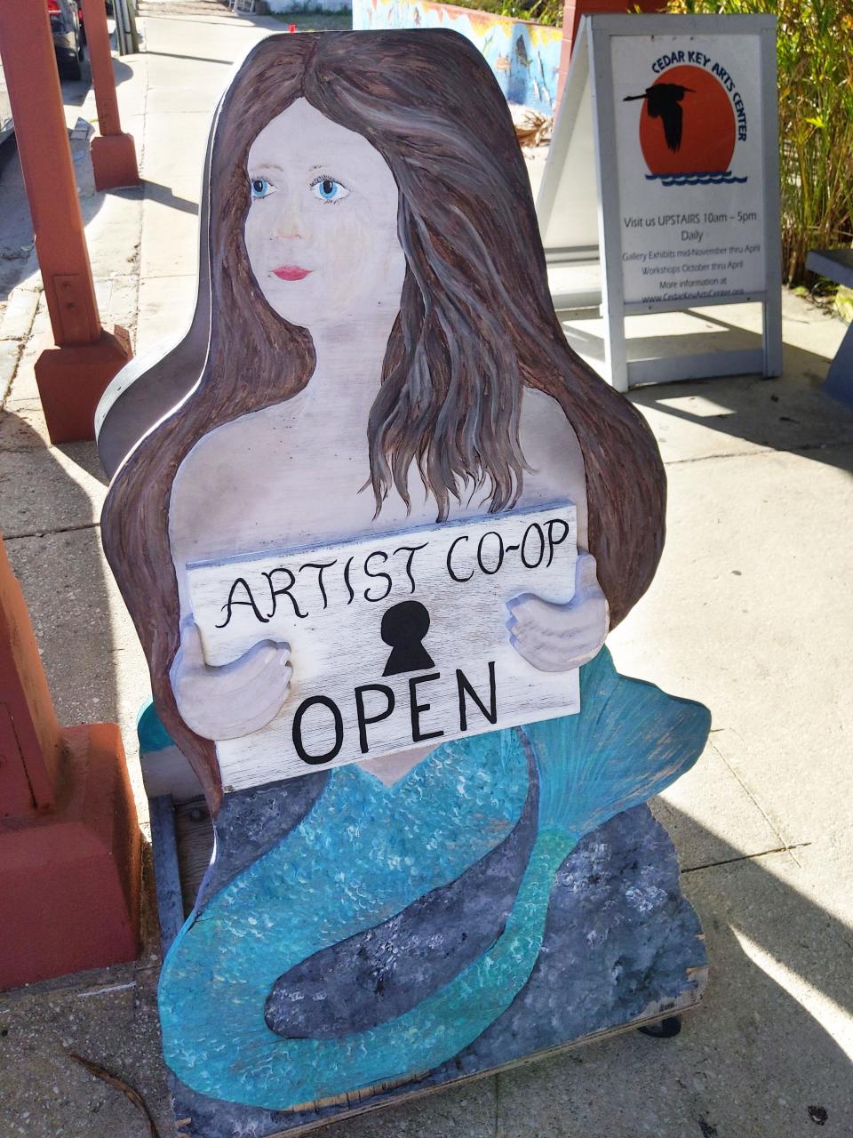 A mermaid sign for an artist coop gallery saying it's open.