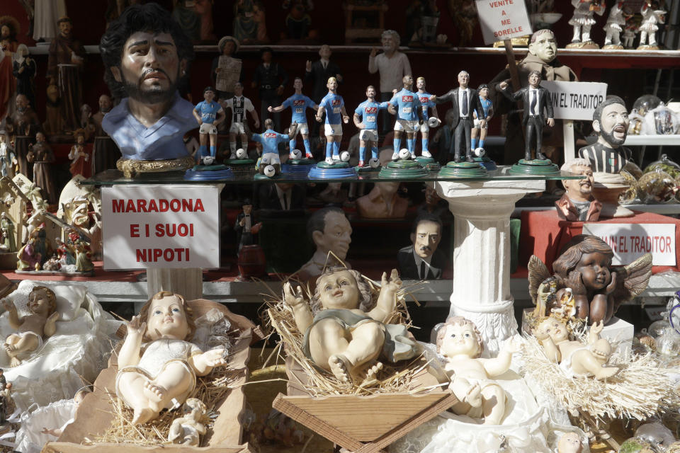 A placard reading Maradona and his nephew is displayed in a shop with the statuettes of soccer legend and former Napoli player Diego Armando Maradona together with nativity scenes ones in Via San Gregorio Armeno, in downtown Naples, Italy, Wednesday, Sept. 18, 2019. Alongside baby Jesus, Mary and Joseph are figurines of Maradona and Dries Mertens. (AP Photo/Gregorio Borgia)