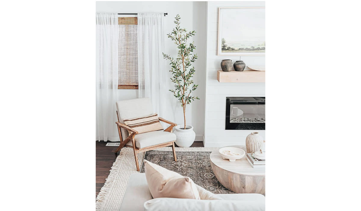 Potted faux olive tree situated between a fireplace and chair in a Scandinavian designed living room. 