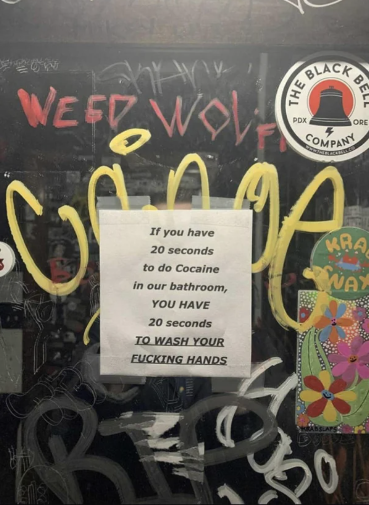 A sign on a wall covered in graffiti says "if you have 20 seconds to do cocaine in our bathroom, you have 20 seconds to wash your fucking hands"