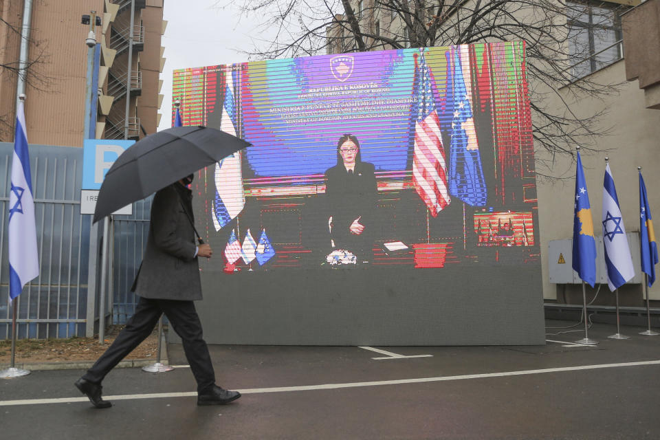 A government official holding an umbrella passes by a monitor displaying Kosovo's Foreign Minister Meliza Haradinaj-Stublla during a signing ceremony held virtually, in the capital Pristina, Monday, Feb. 1, 2021. Kosovo and Israel formally have established diplomatic ties in a ceremony held digitally due to the pandemic lockdown. Kosovo’s Foreign Minister Meliza Haradinaj-Stublla and her Israeli counterpart Gabriel Ashkenazi on Monday held a virtual ceremony signing the documents. The two countries considered it as “making history” and marking “a new chapter.” (AP Photo/Visar Kryeziu)