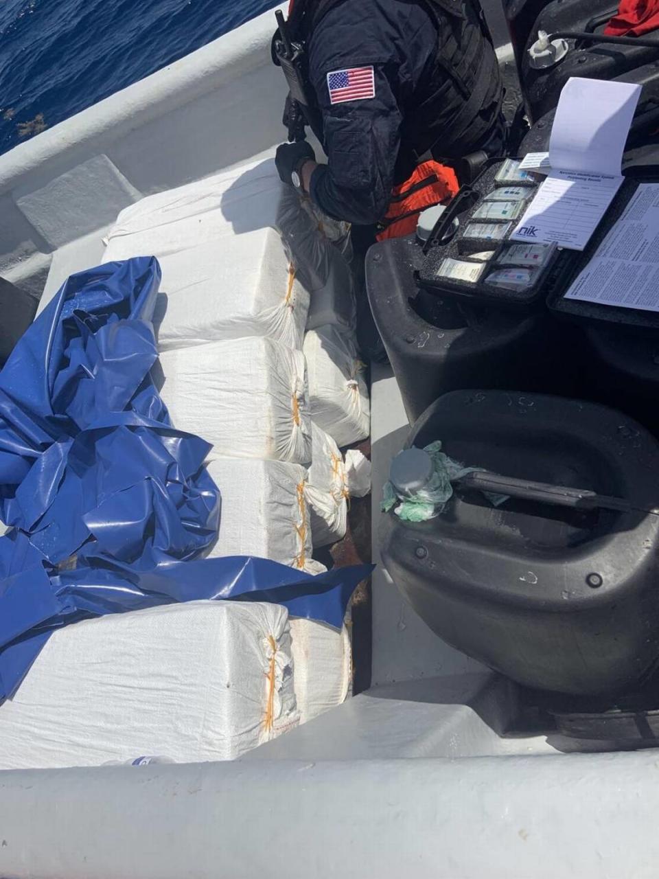 A U.S. Coast Guard crew member stands by a stack of 10 bales of cocaine on board a boat the agency stopped south of the Dominican Republic Wednesday, Sept. 22, 2021.