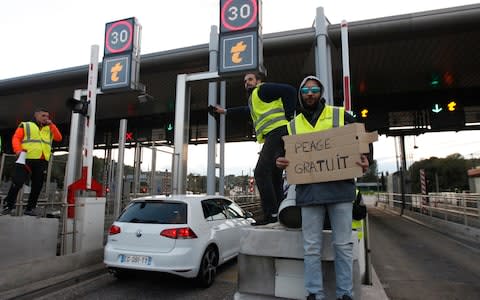 Protesters open toll gates on a motorway in Antibes, as one holds a poster reading "free toll" - Credit: Claude Paris/AP