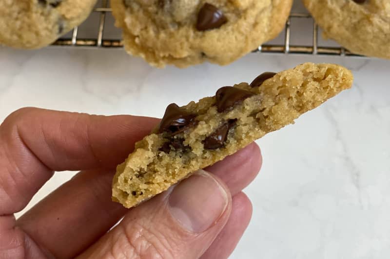 Someone holding soft baked chocolate chip cookie broken in half.