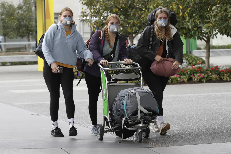 Foreign tourists arrive outside the Christchurch Airport terminal as they prepare to check in for a charter flight back to Germany via Vancouver from Christchurch, New Zealand, Monday, April 6, 2020. The German Embassy in Wellington last week said more than 12,000 German tourists had signed up for its repatriation program from New Zealand following the strict monthlong lockdown, which is aimed at preventing more coronavirus infections. The new coronavirus causes mild or moderate symptoms for most people, but for some, especially older adults and people with existing health problems, it can cause more severe illness or death. (AP Photo/Mark Baker)