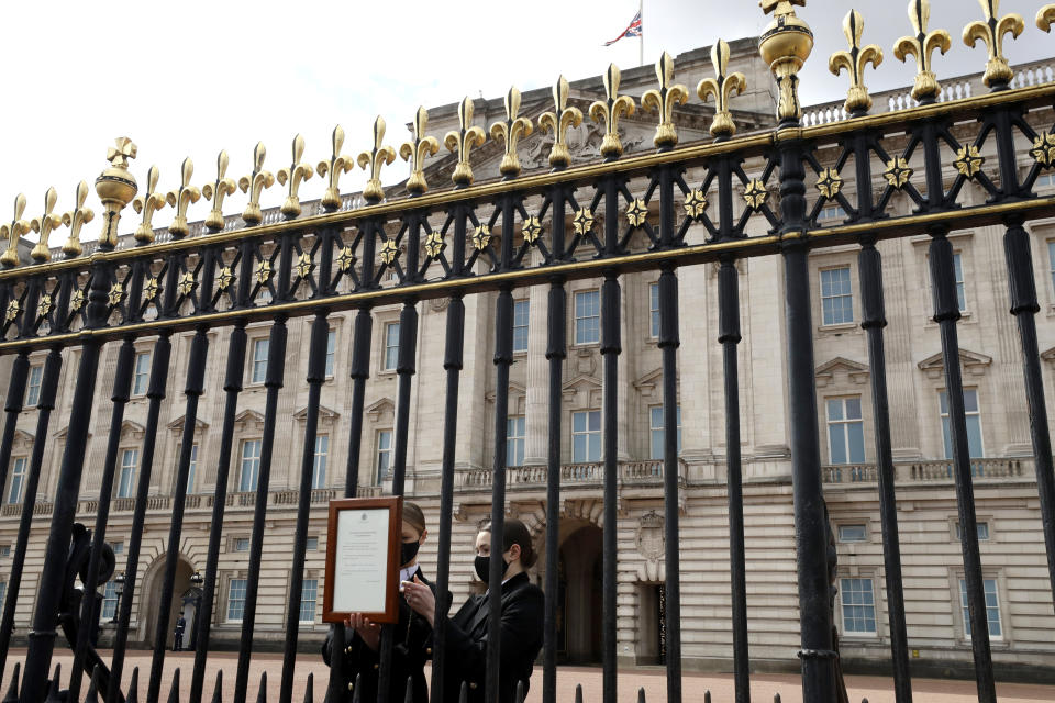 Una bandera de la Unión ondea a media asta mientras personal coloca un anuncio oficial de la muerte del príncipe Felipe en la entrada del Palacio de Buckingham, en Londres, el viernes 9 de abril de 2021. Felipe, el esposo de la reina Isabel II, tenía 99 años. (AP Foto/Matt Dunham)