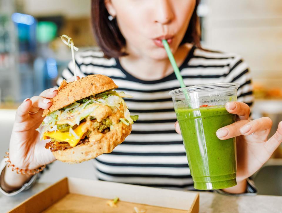 A woman in a vegan restaurant with a plant-based burger and smoothie: Shutterstock