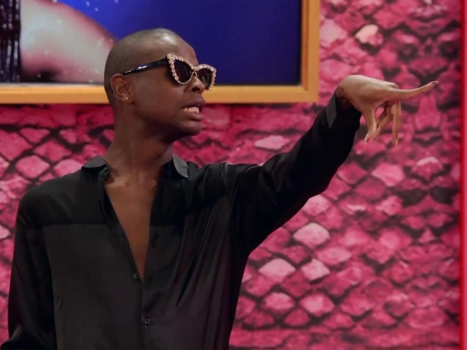 symone reading on drag race with fingers outstretched and wearing sunglasses