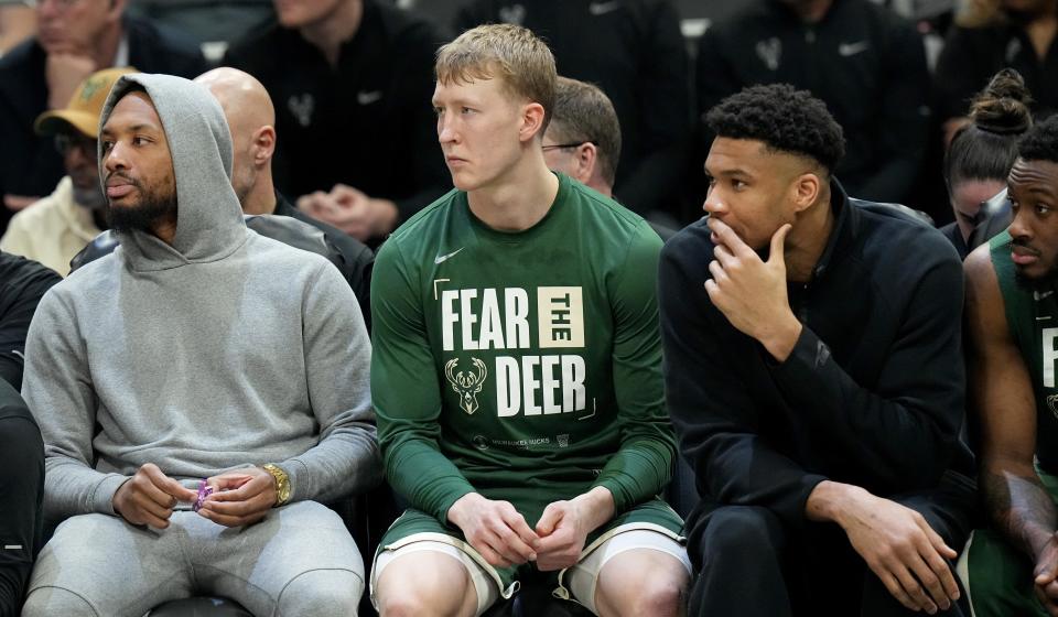 Injured Damian Lillard, left, and Giannis Antetokounmpo flank AJ Green on the bench during a playoff game at Fiserv Forum.