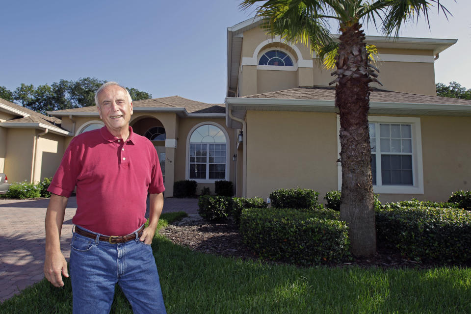 In this Tuesday, July 31, 2012 photo, school teacher Larry Szrom stands in front of his home in Ocoee, Fla. Szrom makes a fraction of what he used to earn, but the former chemical engineer, mortgage broker and real estate developer is thrilled to be working as a high school chemistry teacher, a job he loves. Szrom, a registered Republican who supported John McCain in 2008, is now leaning toward President Barack Obama. He dismisses former Gov. Mitt Romney’s claims that his business skills will get the economy moving. (AP Photo/John Raoux)