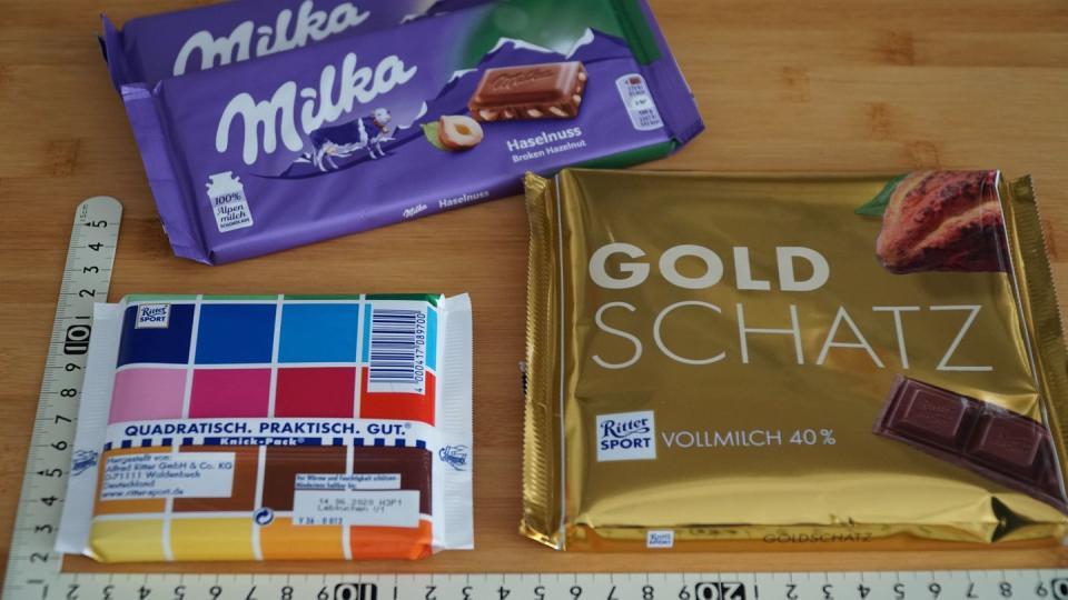 Schokoladentafeln der Marken Ritter Sport und Milka liegen neben einem Maßstab auf einem Tisch.