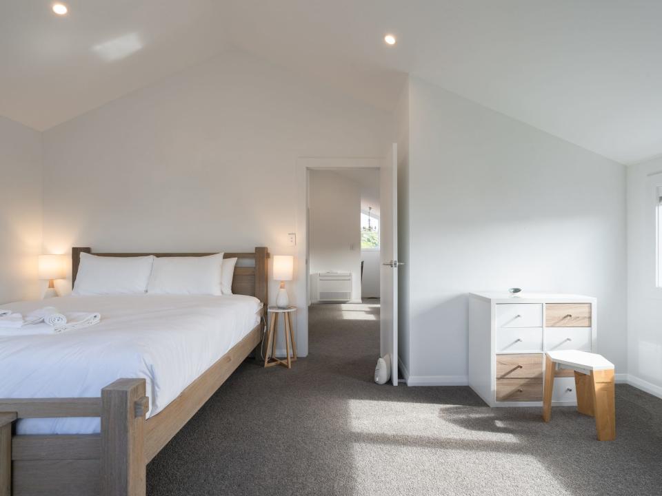 White bedroom with bed with white sheets,  a small night table, and a dresser with white and wood drawers