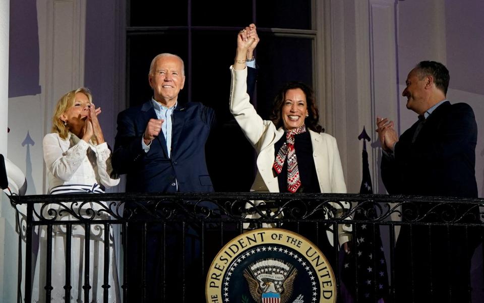 Joe Biden and Kamala Harris hold their joined hands aloft of a balcony at the White Houses, while their spouses applaud them