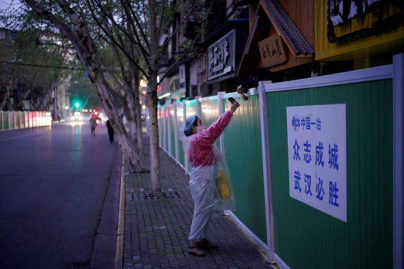 A woman wears a face mask as she shows her phone to a seller to pay for goods over barriers, which have been built to ringfence buildings in Wuhan