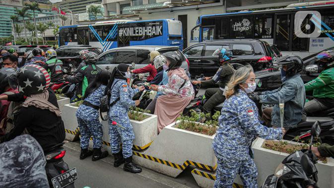 Sejumlah perserta yang tergabung dalam Forum Kader Bela Negara DKI Jakarta membagikan bunga dan masker kepada pengguna jalan di Jalan Thamrin, Jakarta, Rabu (22/12/2021). Aksi tersebut merupakan bentuk apresiasi terhadap kaum perempuan terutama pada peringatan Hari Ibu. (Liputan6.com/Faizal Fanani)