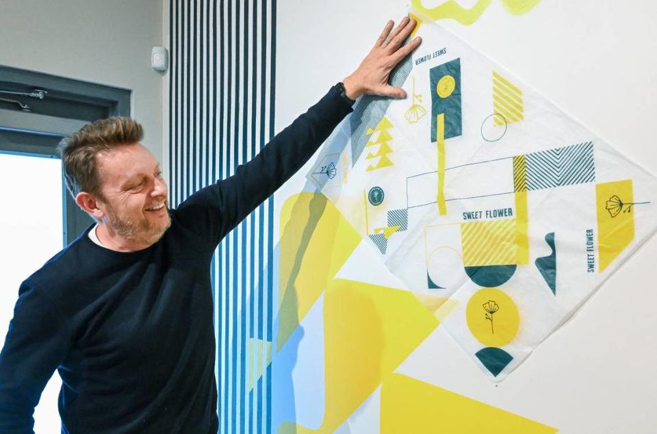 Owner Tim Dodd of the Sweet Flower cannabis dispensary shows a how the design for product wrapping paper was incorporated with the mural design in the new shop opening in the shopping center at Shields and Maroa avenues in central Fresno on Friday, March 29, 2024. CRAIG KOHLRUSS/ckohlruss@fresnobee.com