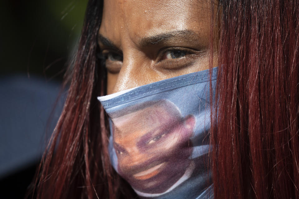 A woman wears a face covering with the likeness of shooting victim Ahmaud Arbery printed on it during a rally to protest Arbery's killing Friday, May 8, 2020, in Brunswick Ga. Two men have been charged with murder in the February shooting death of Ahmaud Arbery, whom they had pursued in a truck after spotting him running in their neighborhood. (AP Photo/John Bazemore)